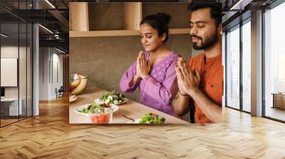 Young indian couple praying before lunch together at home Wall mural