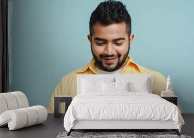 Young indian guy using mobile phone isolated over blue wall Wall mural