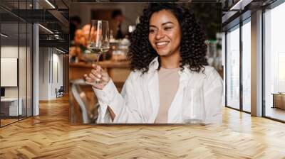 Young joyful african woman drinking wine while dining in restaurant Wall mural