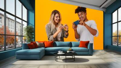 Young loving couple posing isolated over yellow background play games by mobile phones. Wall mural