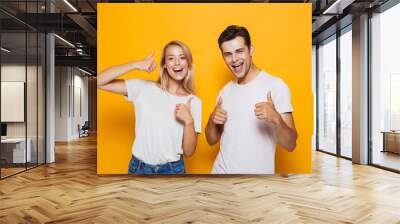 Young loving couple standing isolated over yellow wall background showing thumbs up gesture. Wall mural