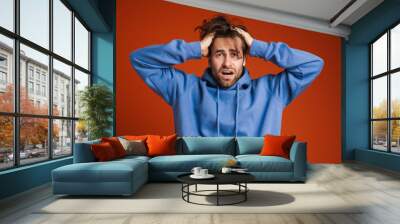 Young man holding his head while expressing surprise Wall mural