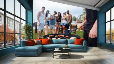 Young man standing and cooking sauseges on barbeque party Wall mural