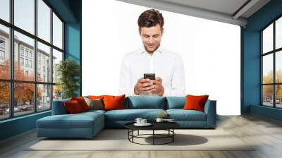 Young man with short dark hair chatting or typing text message with smartphone, isolated over white background Wall mural