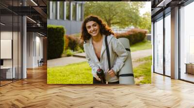 Young middle eastern woman drinking water after yoga practice in park Wall mural