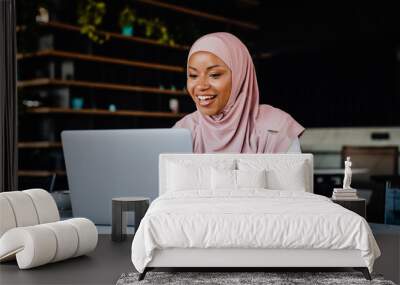 Young muslim woman wearing headscarf working on laptop in office Wall mural