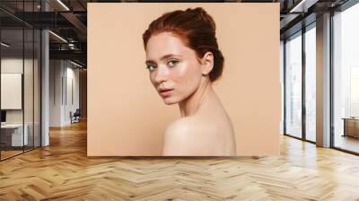 Young redhead woman posing isolated over beige wall background. Wall mural