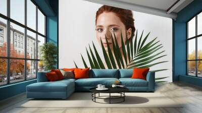 Young redhead woman posing isolated over white wall background with leaf green flowers. Wall mural