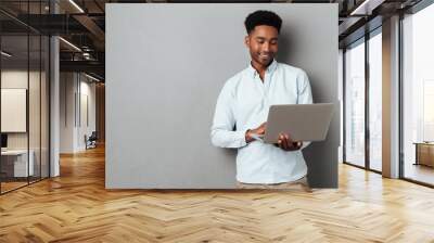 young smiling african man standing and using laptop Wall mural