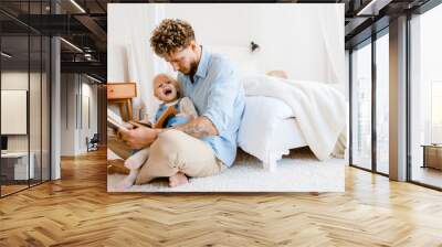 Young white father and little daughter reading book together at home Wall mural