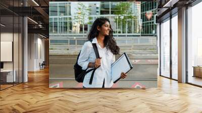 Young woman holding document folder while walking on city street Wall mural