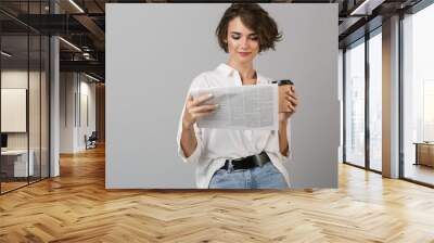 Young woman posing isolated over grey background drinking coffee holding newspaper reading. Wall mural