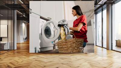 Young woman putting clothes at washing machine while doing laundry Wall mural