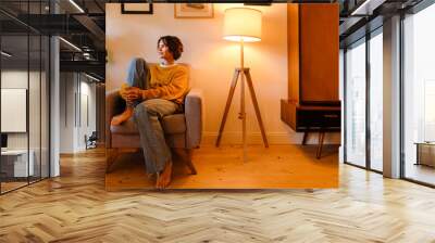 Young woman sitting in armchair while resting at home Wall mural