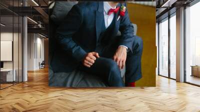 Handsome groom in a wedding tuxedo smiling and waiting for the bride. Rich groom on the wedding day. Elegant groom in a suit and bow tie. The groom suit, holding a lapel of his jacket. Wall mural