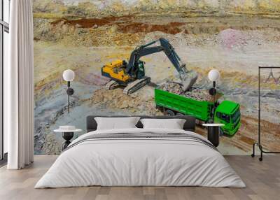 quarrying clay. yellow bulldozer mines clay and loads into green truck. Clay mining process. Wall mural