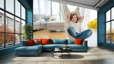 Adorable smiling girl enjoying on indoor swing in bright modern living room Wall mural