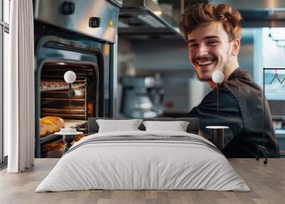 A smiling young man baking homemade pastries in a modern kitchen oven, illustrating home baking and culinary enthusiasm Wall mural