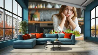 Young woman upset about her salad lunch and sitting at the dinner table Wall mural