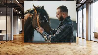 A man strokes a horse. A young bearded farmer takes care of horses. Wall mural