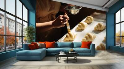 Female baker smears raw croissants with a brush in the yolk, the cooking process. Wall mural