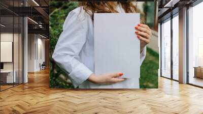 Magazine or book image mockup. Young attractive girl holding a closed book in her hands while standing in the yard. Wall mural