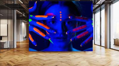 Portrait of beautiful girl with ultraviolet paint on her face. Girl with neon make-up in color light. Wall mural