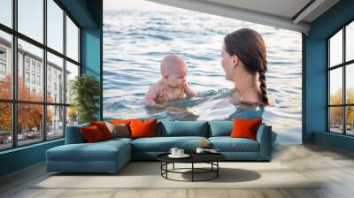 Beautiful young woman with her daughter little baby girl swimming and relaxing in the sea at sunset time Wall mural