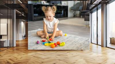 Cute little toddler girl playing at home with eco wooden toys. Happy child cutting vegetables and fruits with toy knife. The child playing educational games.  Wall mural