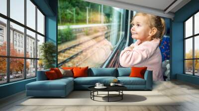 Happy little girl looking out train window outside, while it moving. Traveling by railway in Europe Wall mural