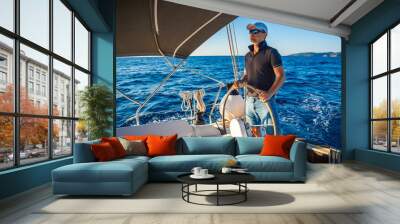 Young man captain stands at the helm and controls a sailboat during a journey by sea Wall mural