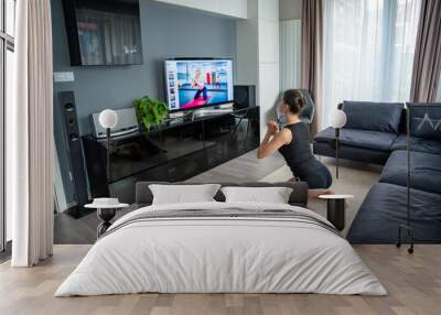 Young woman is doing fitness at home in living room while watching and participating in a class Wall mural