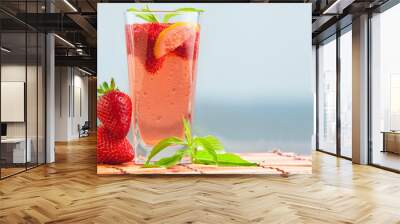 Glass of strawberry lemonade with pieces of strawberry, lemon and fresh mint. Closeup of mojito with beach on background. Fresh summer bright strawberry cocktail. Wall mural