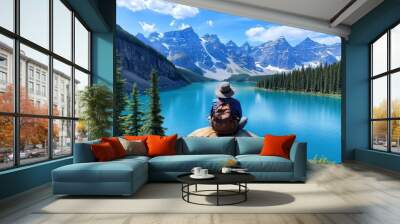 A serene view of a person sitting on a rock, gazing at a stunning turquoise lake surrounded by mountains and evergreen trees. Wall mural