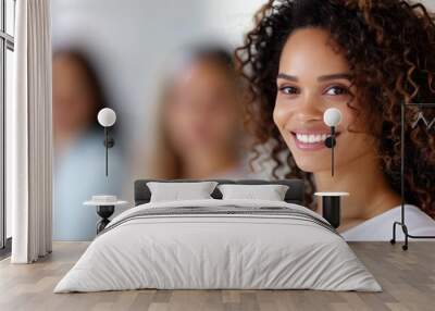 A smiling woman with curly hair stands confidently in the foreground, with two blurred individuals behind her, exuding positivity and warmth. Wall mural