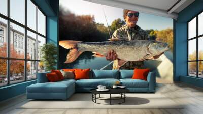 Happy fisherman holds the trophy Asp fish (Leuciscus aspius) and smiles. Tilt shift effect applied Wall mural