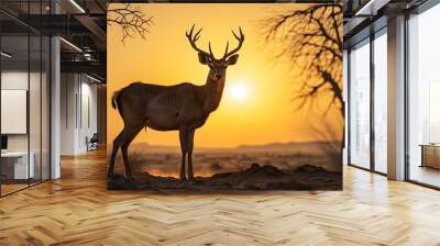 Majestic deer amidst a dramatic desert landscape at sunset, framed by barren trees and a stunning golden sky Wall mural