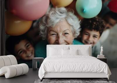 A cheerful elderly woman is surrounded by joyful children and bright balloons, symbolizing the blissful moments in life and the bonds between generations. Wall mural