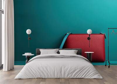 A chic red clutch bag adorned with a blue strap is placed on a teal background, highlighting the simple yet striking color juxtaposition and minimalist design of the accessory. Wall mural