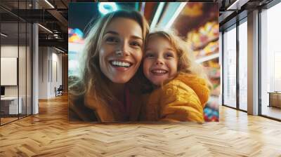 A joyful mother and her young daughter capture a precious moment together, smiling broadly at a vibrant and colorful night market illuminated by bright lights. Wall mural