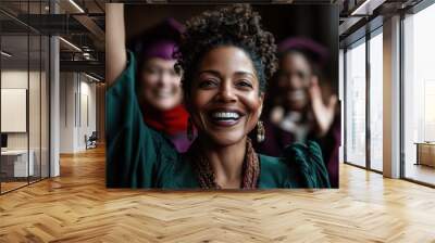 A joyful woman with curly hair celebrates her graduation, smiling broadly among classmates, capturing a moment of achievement and happiness in vibrant surroundings. Wall mural