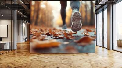 A person runs along a serene path covered with orange and brown autumn leaves in a beautiful, sunlit forest, capturing a sense of motion and tranquility in nature. Wall mural