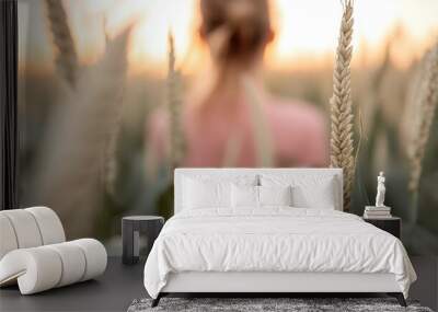 A person stands amidst golden wheat stalks under the warm glow of a sunset, symbolizing peace, freedom, and the timeless connection between humans and the earth. Wall mural