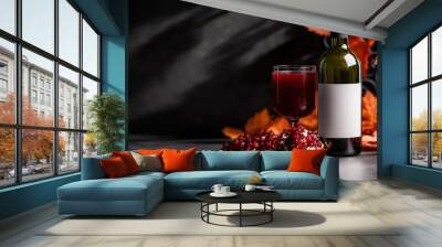 A sophisticated setting of a bottle and glass of red wine accompanied by vibrant autumn leaves and an open pomegranate, evoking a sense of rich harvest warmth. Wall mural