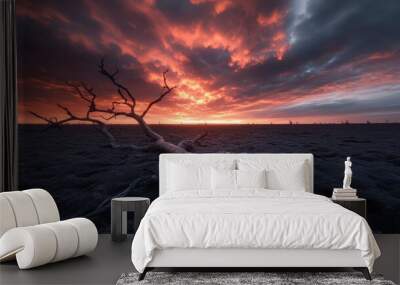 A stunning sunset casts a vibrant glow over a scene of cracked ground, where a fallen branch lies, creating a mesmerizing and evocative depiction of nature's contrast. Wall mural