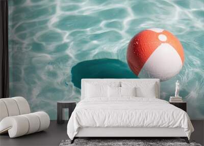 A vibrant red and white beach ball floats effortlessly on the rippling clear blue waters of a swimming pool, embodying the essence of summer fun and relaxation. Wall mural