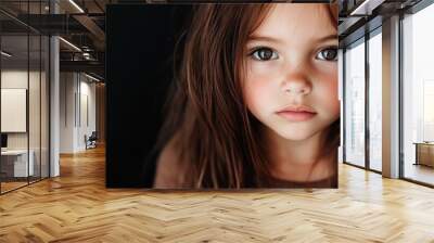 A young girl with freckles and big blue eyes gazes adoringly at the viewer, conveying innocence and purity against a minimalist dark background. Wall mural