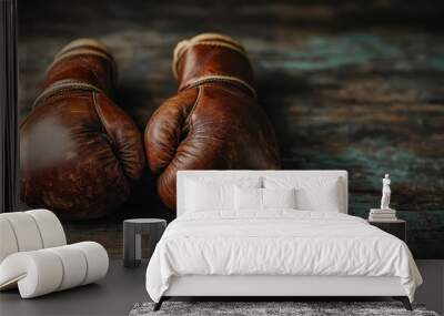 Close-up of a pair of well-used vintage brown leather boxing gloves resting on worn wooden boards, representing the toughness and dedication inherent in the sport of boxing. Wall mural