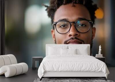 Close-up of a thoughtful bearded man wearing glasses, conveying a sense of focus and contemplation within a soft, blurred background that enhances modern elegance. Wall mural