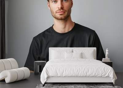 A man with a beard and brown hair is wearing a black t-shirt. He is standing in front of a white wall Wall mural